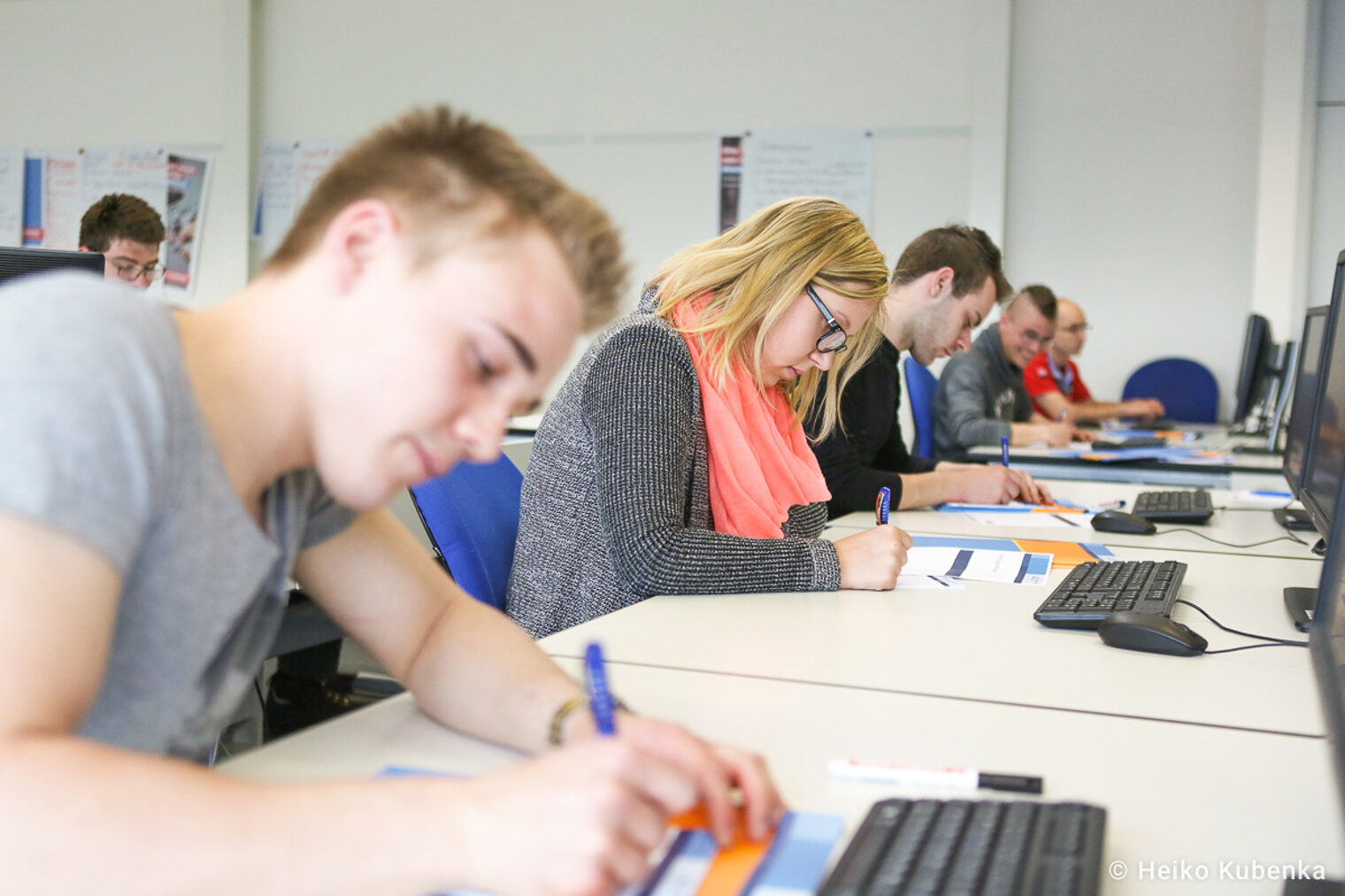 Teilnehmende eines Seminars schreiben auf Arbeitsblätter Auszubildende nehmen an einem Seminar teil und schreiben auf Arbeitsblätter, während sie vor Computern sitzen.