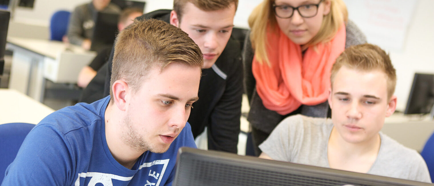 Personen vor Computer-Bildschirm In einem Unterrichtsraum stehen vier Personen und gucken gemeinsam auf einen Computer-Bildschirm.