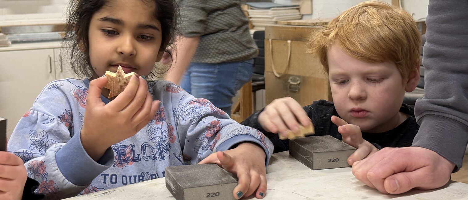 Zwei Kindergartenkinder blicken in einer Werkstatt stolz auf ihre selbst gemachten Holzsterne.